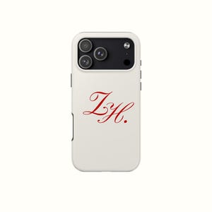 May include: White phone case with a red script design of the letters "ZH." The case has a black camera module with three lenses and a flash. The case is designed to fit a smartphone.