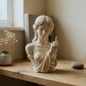 May include: A cream-coloured bust sculpture of a person with wavy hair, draped in fabric, with one hand raised showing the middle finger. The figure has a smooth, matte finish and is depicted from the chest up, showcasing detailed facial features.