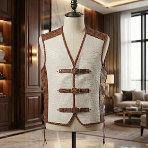 Op de afbeelding: Een witte vest met krokodillenstructuur, bruine randen en decoratieve gespen. De vest heeft bruine slangenleeraccenten op de schouders en zijkanten. De vest wordt op een mannequin gepresenteerd.