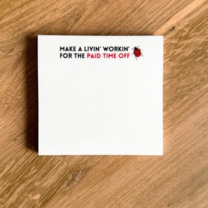 May include: A square white notepad featuring the black text MAKE A LIVIN' WORKIN' FOR THE and the red text PAID TIME OFF, accompanied by a small red and black ladybug illustration positioned to the right of the printed text.