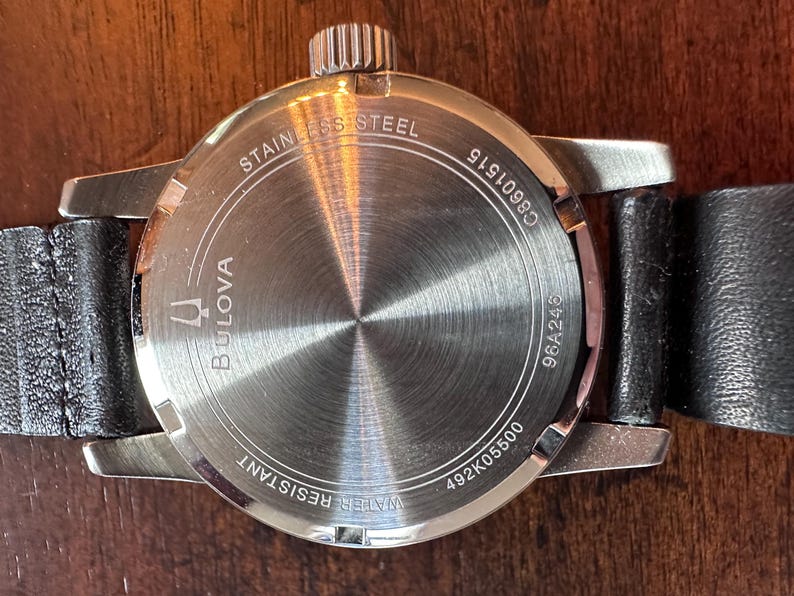 May include: A stainless steel Bulova watch with a black leather strap. The watch back is visible, displaying the brand name, model numbers, and the words "Water Resistant" and "Stainless Steel".
