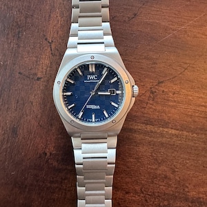 May include: A stainless steel wristwatch with a blue dial. The watch features the brand name "IWC SCHAFFHAUSEN" and the word "INGENIEUR" on the dial. The watch has a silver metal strap and a date display.