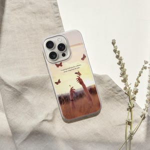 May include: A clear phone case with a nature-themed design. The case features a graphic of hands reaching for butterflies in a field, with text that reads "I'm going kind of crazy for a flower, always rising from the ashes."