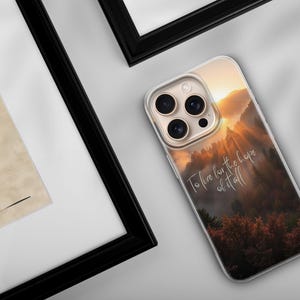 May include: A clear phone case featuring a scenic mountain landscape with a sunset and the text "To live for the hope of it all." The case is on a white surface next to a framed artwork.