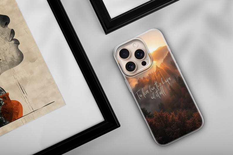 May include: A clear phone case featuring a scenic mountain landscape with a sunset and the text "To live for the hope of it all." The case is on a white surface next to a framed artwork.