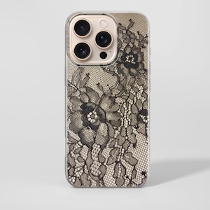 Puede incluir: Una funda transparente para teléfono con un diseño de encaje floral negro. El intrincado patrón de encaje cubre la parte posterior de la funda del teléfono, creando una estética delicada y elegante. La funda tiene un anillo de cámara dorado.