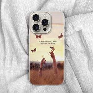 May include: A phone case featuring a sunset scene with butterflies and outstretched arms. The case has a quote: "I'm getting tired even for a phoenix, always rising from the ashes."