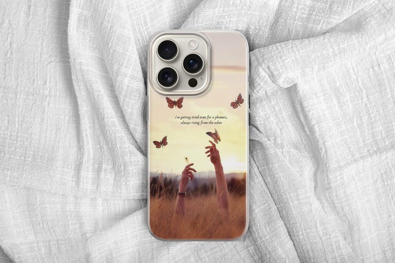 May include: A phone case featuring a sunset scene with butterflies and outstretched arms. The case has a quote: "I'm getting tired even for a phoenix, always rising from the ashes."