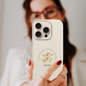 May include: A cream-colored phone case with a floral design and the word "fearless" in a script font. The case has a clear border and a camera cutout. The design includes the text "but with you I'd dance in a storm in my best dress."