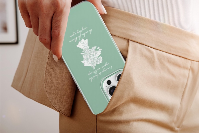 May include: A mint green phone case with a floral design and script. The case is in a pocket of tan pants. The script reads: "I always like to think the flowers are awake at night, everything a dream."