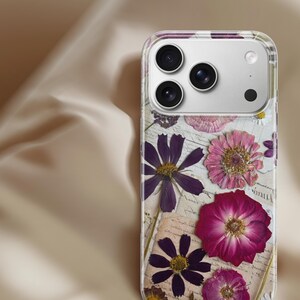 Puede incluir: Funda transparente para teléfono con flores prensadas en tonos morado, rosa y amarillo. Las flores están dispuestas sobre un fondo de papel vintage, creando un diseño único y artístico.