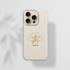 May include: A beige phone case with a floral design and the word "fearless" in a script font. The design includes a circle of text that reads "but with you I'd dance in a storm in my best dress". The phone case has a clear border.