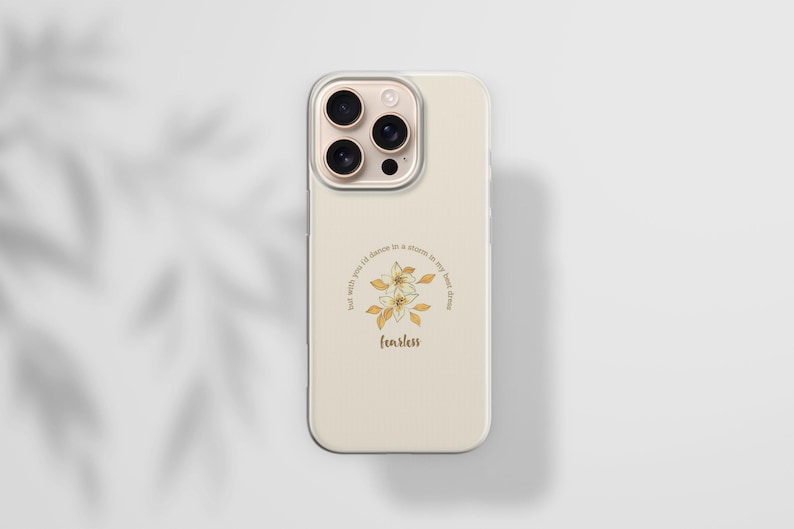 May include: A beige phone case with a floral design and the word "fearless" in a script font. The design includes a circle of text that reads "but with you I'd dance in a storm in my best dress". The phone case has a clear border.