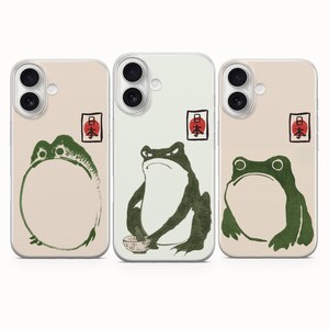 Peut inclure: Trois coques de téléphone ornées d'illustrations de grenouilles vertes dans un style à l'encre. Chaque coque présente un petit tampon avec des caractères japonais rouges et noirs. Les grenouilles sont représentées dans diverses postures.