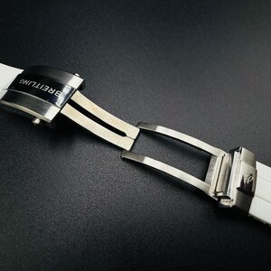 Puede incluir: Primer plano de una correa de reloj blanca con un cierre plateado. El cierre est&aacute; grabado con la marca "Breitling" en negro. La correa est&aacute; hecha de un material suave y flexible.