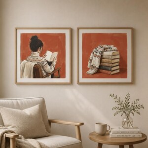 May include: Two square framed wall art prints featuring a burnt orange background. The left print shows a person in a patterned jumper reading a book. The right print depicts a stack of books topped with a folded patterned jumper.
