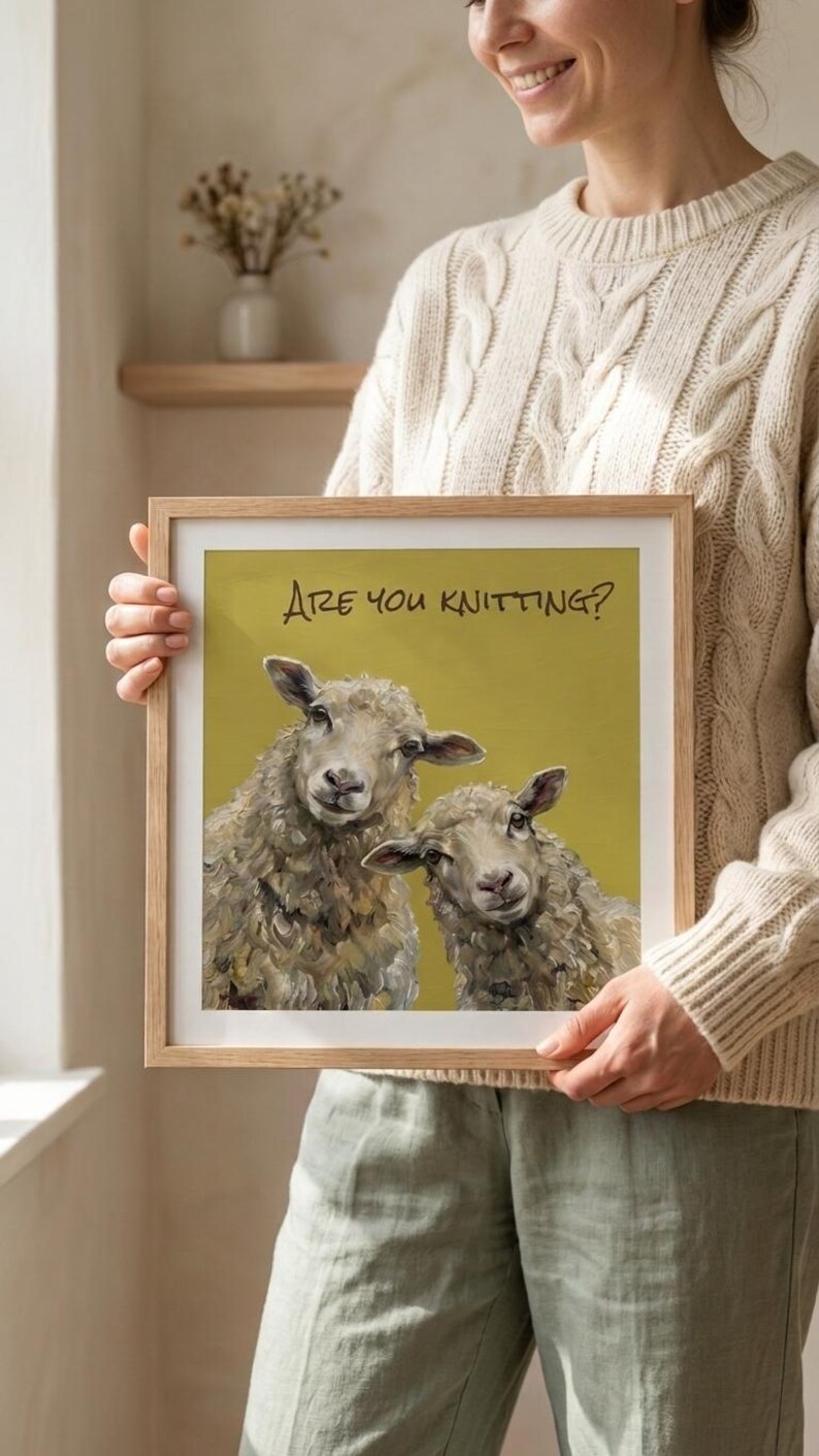 May include: A square framed print featuring an oil painting of two sheep against a mustard yellow background. The text "ARE YOU KNITTING?" is printed in black at the top. The sheep have textured, off-white wool and are looking forward.