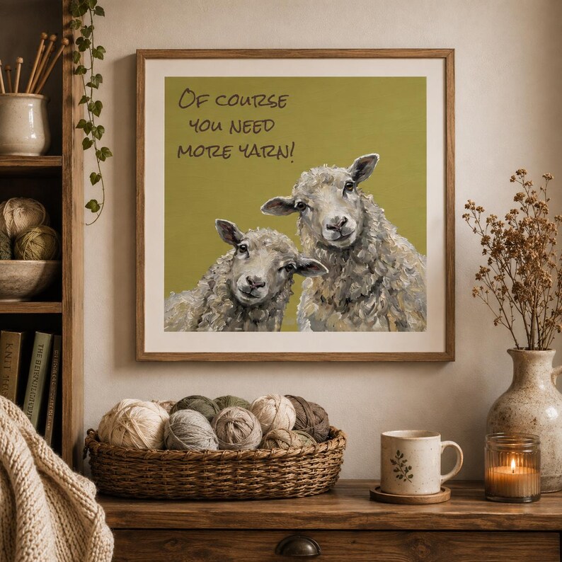 May include: A square framed wall art print featuring an olive green background with two sheep and the text "Of course you need more yarn!" in black lettering. The sheep are rendered in shades of gray, white, and brown with visible brushstrokes.