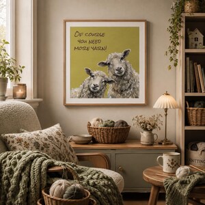 May include: A square framed wall art print featuring two sheep against a mustard yellow background with the black text Of course you need more yarn! The artwork is displayed in a room with a green armchair, a wooden side table, and a bookshelf.
