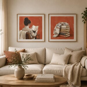 May include: Two square framed wall art prints featuring a burnt orange background. The left print shows a person in a patterned sweater reading a book. The right print depicts a stack of books topped with a folded patterned sweater.