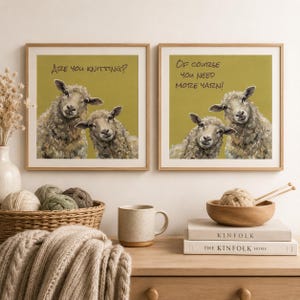May include: Two square framed wall art prints with light wood frames. The left print shows two sheep on a mustard background with the text Are you knitting? The right print shows two sheep on a mustard background with the text Of course you need more yarn!