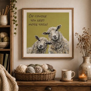 May include: A square framed wall art print featuring an olive green background with two sheep and the text "Of course you need more yarn!" in black lettering. The sheep are rendered in shades of gray, white, and brown with visible brushstrokes.