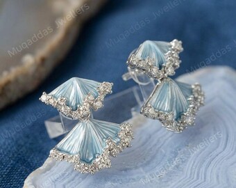 May include: A pair of stud earrings featuring two fan-shaped elements in light blue enamel, accented with small clear stones along the edges. The design consists of a smaller top fan and a larger bottom fan connected together in a metallic setting.