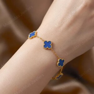 May include: A gold chain bracelet featuring four evenly spaced blue clover-shaped charms with gold borders. The bracelet is delicate and consists of a thin link chain connecting each of the four-leaf clover motifs in a repeating pattern.
