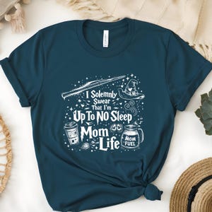 May include: Teal t-shirt with a white graphic design. The design includes a wand, a witch's hat, a coffee cup, and a milk jug with the words "I Solemnly Swear That I'm Up To No Sleep Mom Life" and "Mom Fuel".