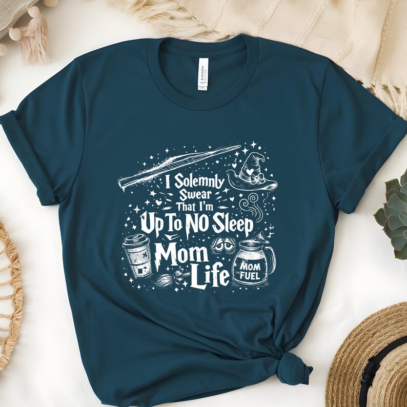 May include: Teal t-shirt with a white graphic design. The design includes a wand, a witch's hat, a coffee cup, and a milk jug with the words "I Solemnly Swear That I'm Up To No Sleep Mom Life" and "Mom Fuel".