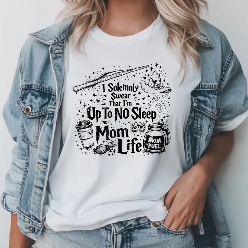 May include: White t-shirt with a black graphic design featuring a wand, witch hat, coffee cup, and the text "I Solemnly Swear That I'm Up To No Sleep Mom Life". The shirt is paired with a denim jacket.