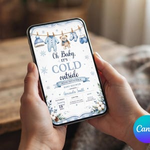 May include: A digital baby shower invitation displayed on a smartphone screen featuring a winter theme with blue baby clothes hanging on a line, a teddy bear, snowflakes, and the text Oh Baby, IT'S COLD outside, Amanda Smith, and event details.