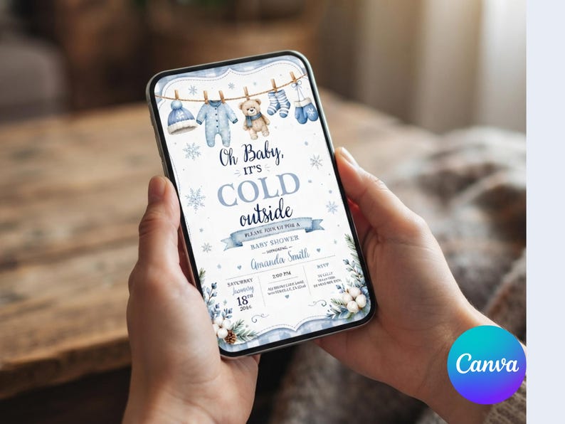 May include: A digital baby shower invitation displayed on a smartphone screen featuring a winter theme with blue baby clothes hanging on a line, a teddy bear, snowflakes, and the text Oh Baby, IT'S COLD outside, Amanda Smith, and event details.