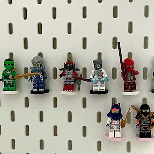 May include: A collection of colorful Lego Ninjago minifigures, each with unique armor and accessories. The figures are displayed on a white pegboard, showcasing a variety of ninja characters in vibrant colors like red, green, and blue.