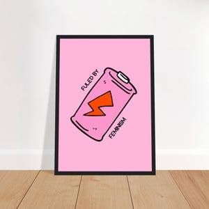 Könnte beinhalten: Gerahmter rosa Druck mit einem Cartoon-Batterie-Design. Die Batterie hat einen orangefarbenen Blitz und den Text „FUELED BY FEMINISM“. Die Batterie ist schwarz umrandet, der Rahmen ist schwarz.