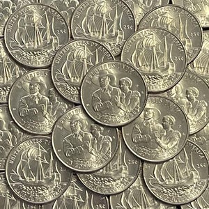 May include: A collection of silver quarter coins. Some coins feature a sailing ship, while others depict a man and woman. The coins are marked with "United States of America" and "25¢".