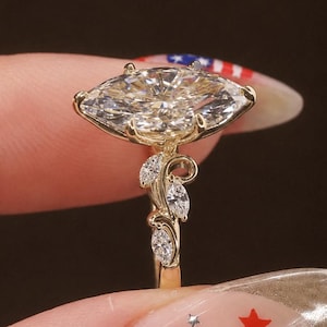 Puede incluir: Un anillo de oro con una gran piedra central de talla marquesa sujeta por garras. La banda está decorada con una serie de piedras más pequeñas de talla marquesa dispuestas en un patrón de hojas a lo largo de los lados del engaste.