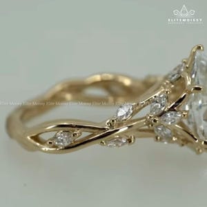 May include: A gold-colored engagement ring with a large, clear, marquise-cut center stone. The band features a delicate, intertwined design with smaller, marquise-cut accent stones. The ring has a nature-inspired, floral theme.
