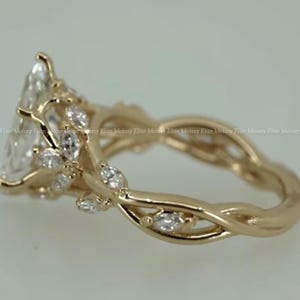 May include: A gold-colored engagement ring with a pear-shaped center stone and smaller accent stones. The band features a twisted vine design with leaf-like details, creating a nature-inspired aesthetic.