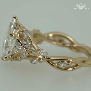 May include: A gold-colored ring with a pear-shaped, clear gemstone as the centerpiece. The ring features a delicate, vine-like design with smaller, marquise-cut gemstones and intricate detailing. The band has a twisted design.