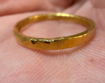 May include: Close-up of a gold ring with a textured surface. The ring is a simple band design, showcasing a warm, yellow-gold color. The ring's surface has a slightly hammered or hand-crafted appearance.