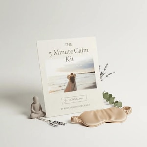 Könnte beinhalten: Eine beige Augenmaske, eine kleine sitzende Buddha-Statue und eine Karte mit dem Text "The 5 Minute Calm Kit" sind auf einer weißen Oberfläche angeordnet. Die Karte zeigt eine Strandszene und das Wort "DOWNLOAD".