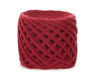 May include: A cylindrical spool of deep red fabric yarn. The yarn is tightly woven in a lattice pattern, creating a textured surface. The yarn appears soft and pliable, suitable for various crafting projects. The overall shape is a compact, rounded cylinder.