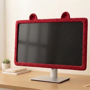 Puede incluir: Una funda de ganchillo de color rojo oscuro para monitor de ordenador con dos pequeñas orejas redondeadas en el borde superior. La funda enmarca la pantalla rectangular de un monitor montado sobre un soporte plateado. Se aprecia la textura.