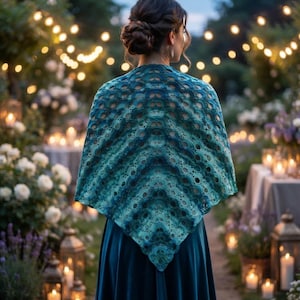 May include: A triangular crochet shawl featuring a gradient of teal, turquoise, and deep blue hues with an intricate openwork fan pattern. The shawl is draped over the shoulders, showcasing a textured, scalloped edge and a pointed bottom hem.