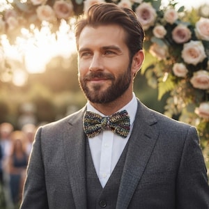 Puede incluir: Una chaqueta de traje gris carbón sobre una camisa blanca de botones y una pajarita de punto texturizada y multicolor con motas de hilo verde, azul y amarillo. El conjunto se completa con un chaleco a juego de color gris carbón.