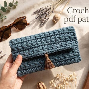 May include: A blue rectangular crochet clutch featuring a textured star stitch pattern and a small brown tassel attached to the center flap. The text "Crochet pdf pattern" is visible in the upper right corner of the image.