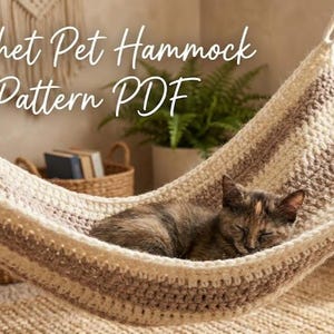 May include: A crocheted pet hammock in cream and brown stripes, with a sleeping cat inside. The text "Crochet Pet Hammock Pattern PDF" is written across the top. The hammock is suspended in a room with a woven rug.