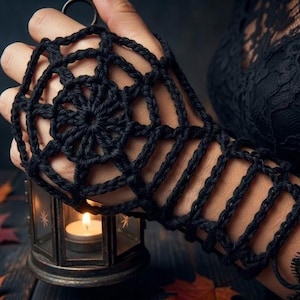 May include: A black crochet fingerless glove featuring a spiderweb pattern on the back of the hand and a series of horizontal loops extending down the wrist. The yarn is dark and textured, creating an openwork design that covers the hand.