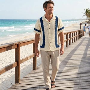 Può includere: Una camicia a maniche corte in crochet color crema con chiusura frontale a bottoni e strisce verticali blu navy sul petto e sulle maniche, abbinata a pantaloni beige chiaro e sandali in pelle marrone con due cinturini regolabili.